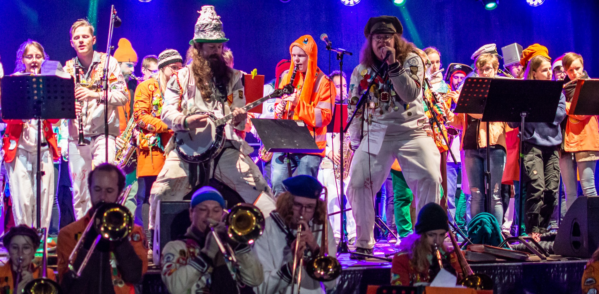 Orkestern Wijkmanska Blecket uppträder på scen med blåsare, banjo och sångare i färgglada overaller och scenkläder