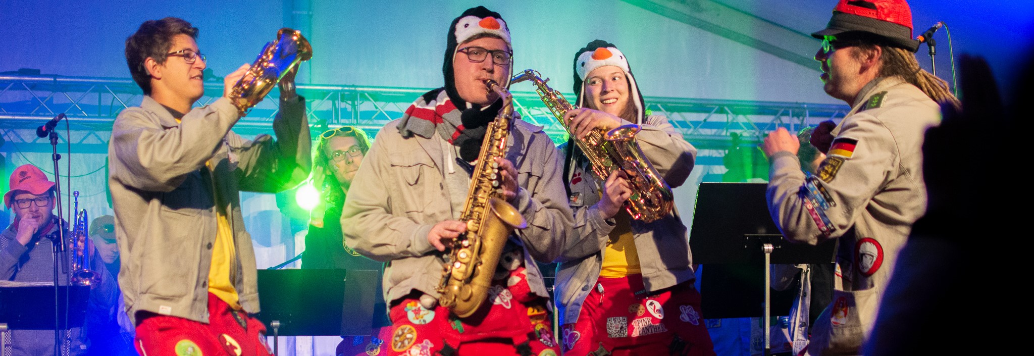 Orkestern ACO uppträder på scen i röda overaller och ljusa jackor, med musiker som spelar saxofon under färgglada scenljus